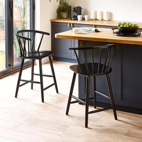 Two black wooden bar stools with rounded spindle backrests by a kitchen island with wood countertop