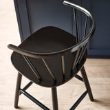 Close-up angled view of black wooden bar stool rounded spindle backrest and seat on wood floor