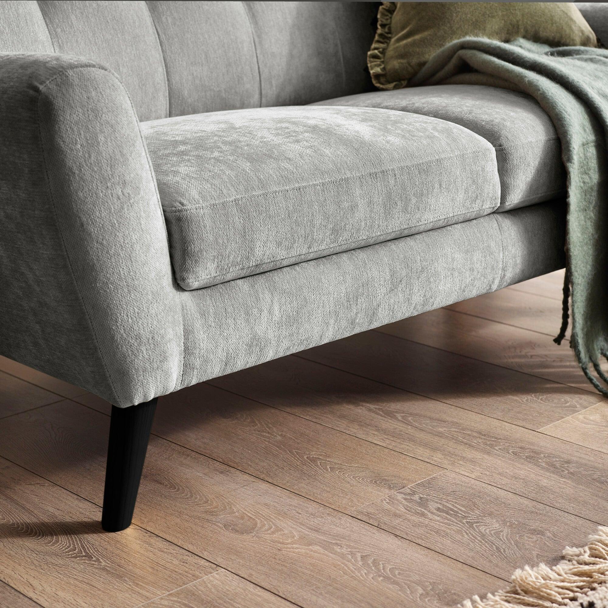 Light grey fabric sofa with black angled legs and green throw on wooden floor