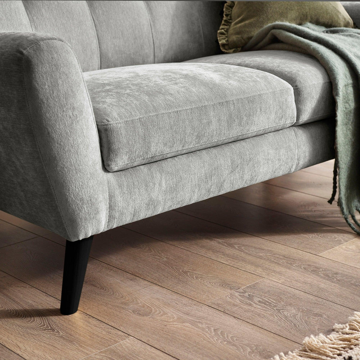 Light grey fabric sofa with black angled legs and green throw on wooden floor