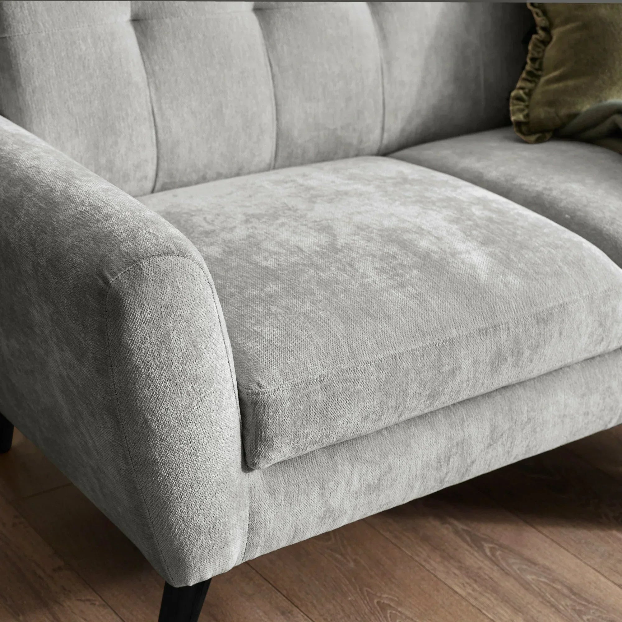 Light grey fabric sofa close-up showing cushioned seat, armrest and wooden legs on hardwood floor