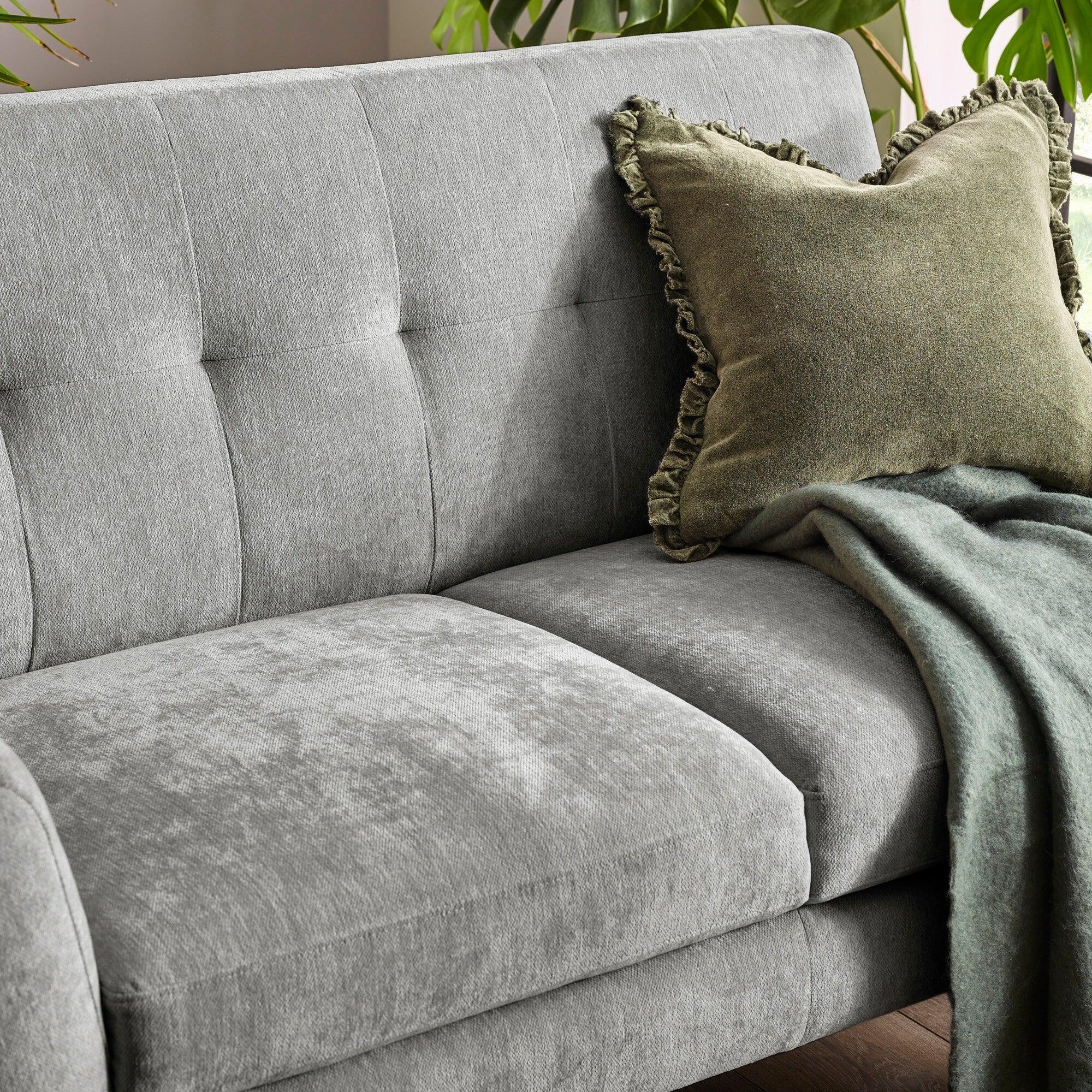 Grey fabric sofa with square tufted back, olive ruffle cushion and soft green throw blanket