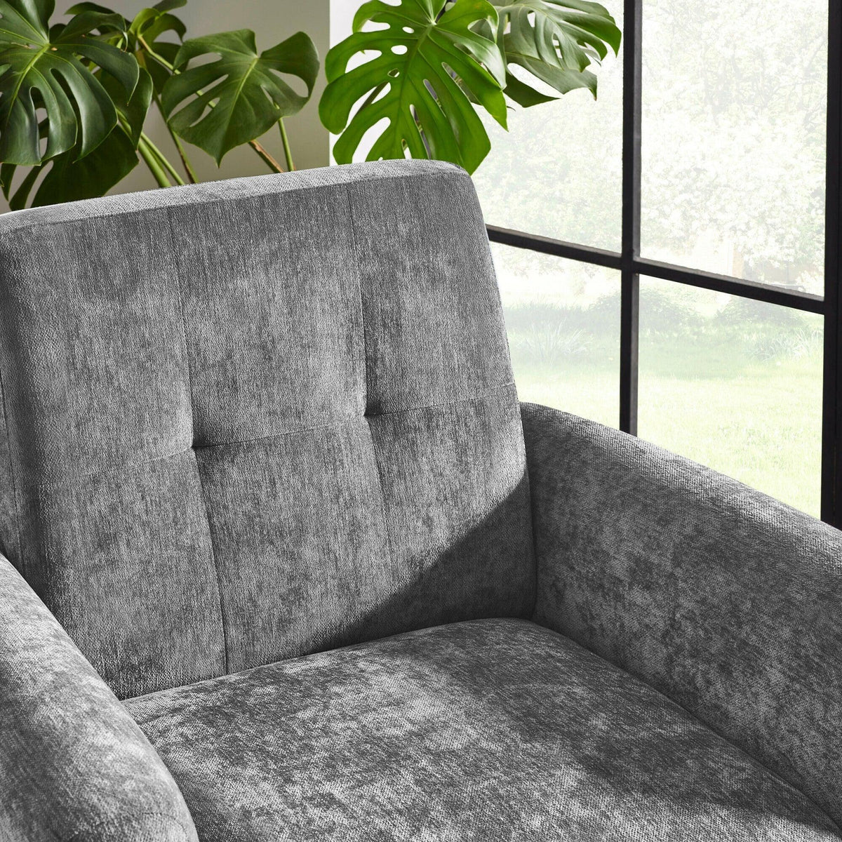 Grey fabric sofa armchair with tufted backrest near window and green indoor plants
