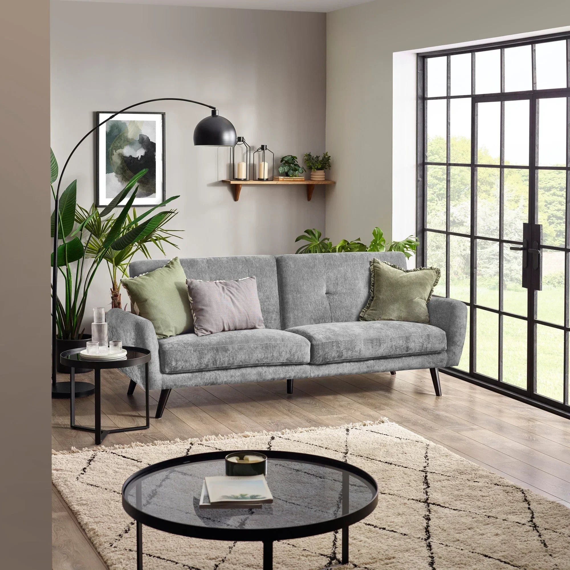 Dove grey sofa bed in modern living room with plants, round tables and large window