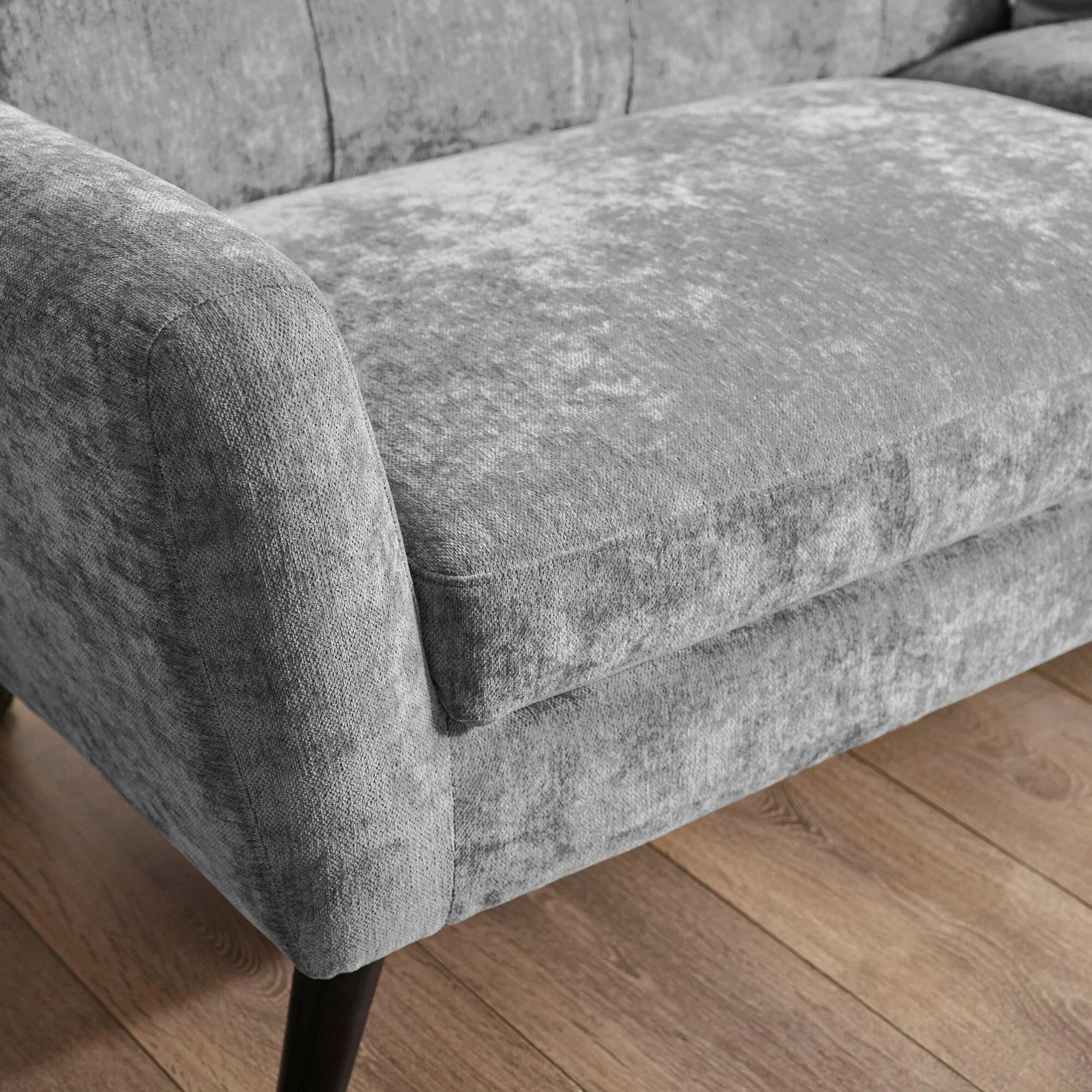 Close-up of grey fabric sofa arm and seat with wooden legs on oak flooring