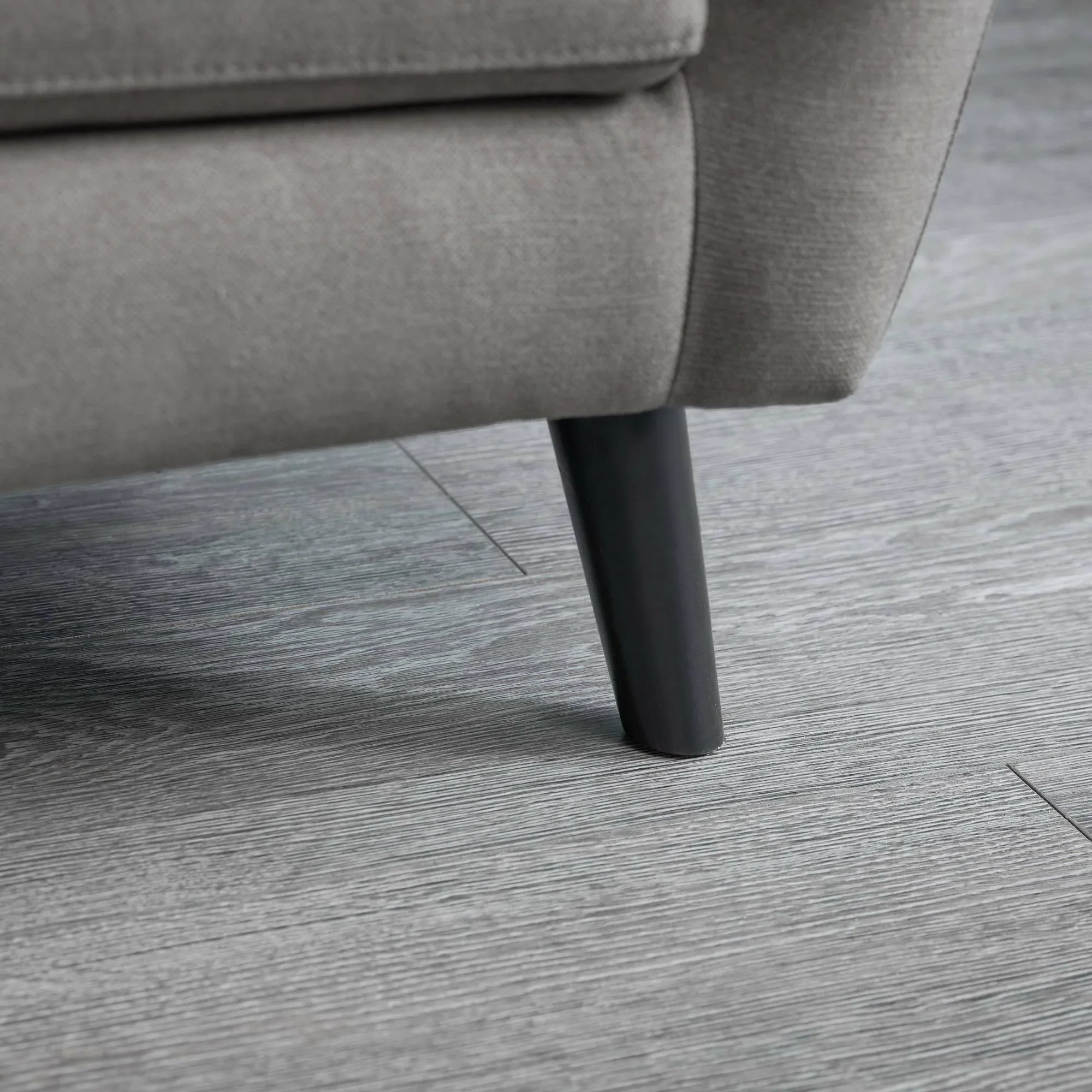 Monza chair detail showing grey fabric upholstery and black leg on wood flooring