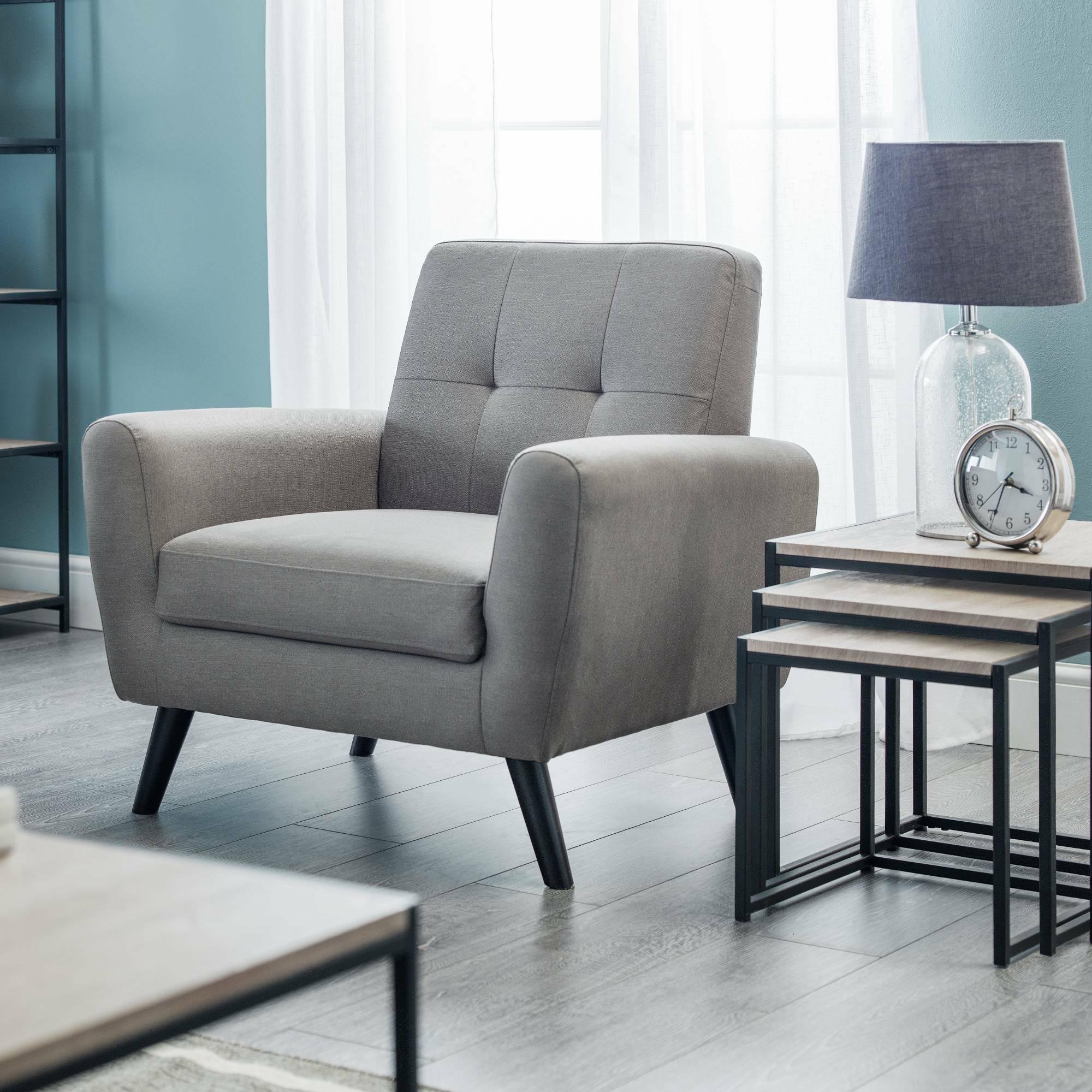 Grey upholstered accent chair with black legs in modern living room beside nesting tables