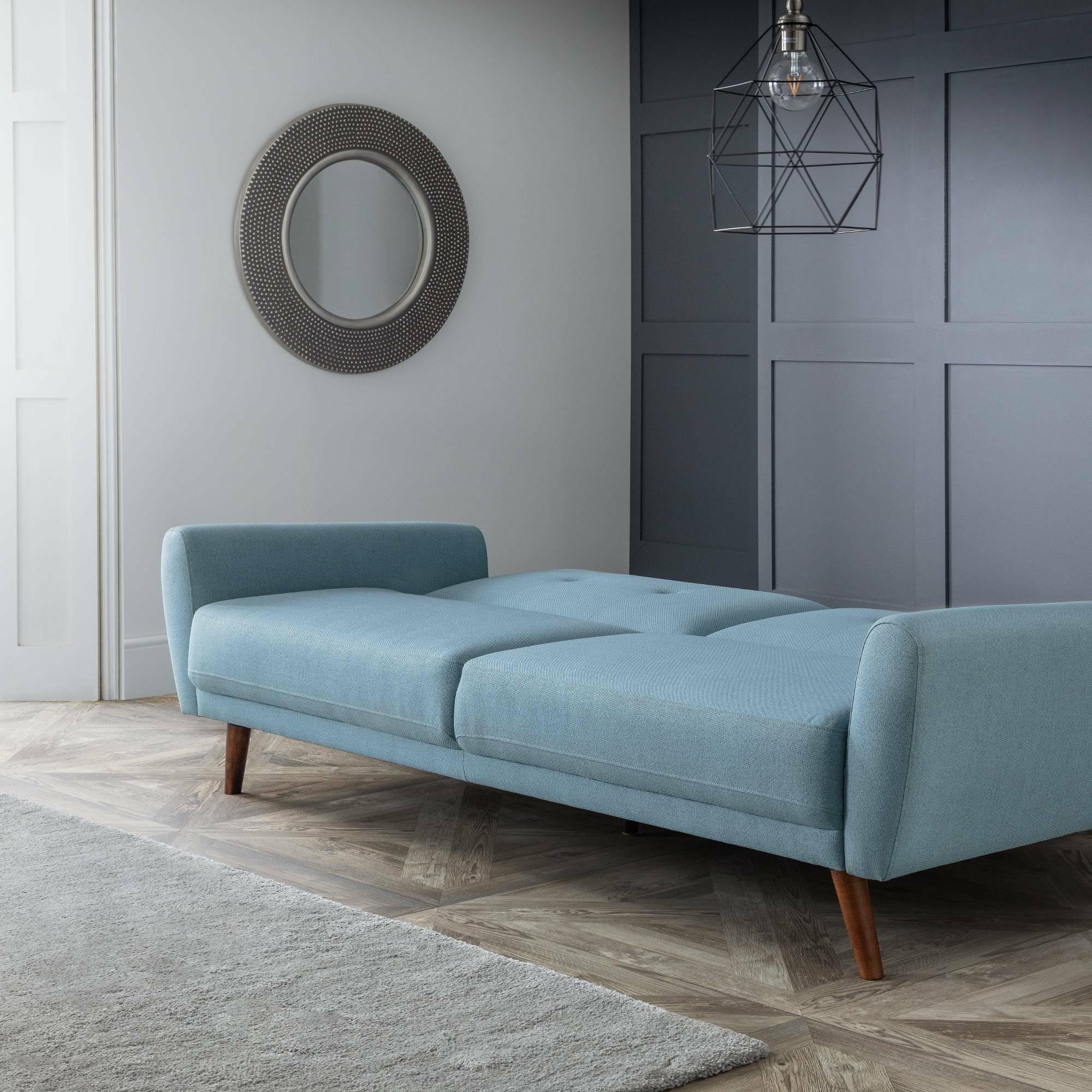 Blue sofabed with wooden legs in a modern living room with grey walls and round mirror