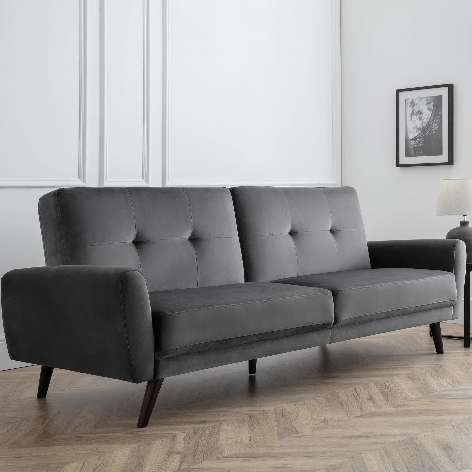 Grey velvet sofabed with button-tufted backrest in modern living room with wood flooring