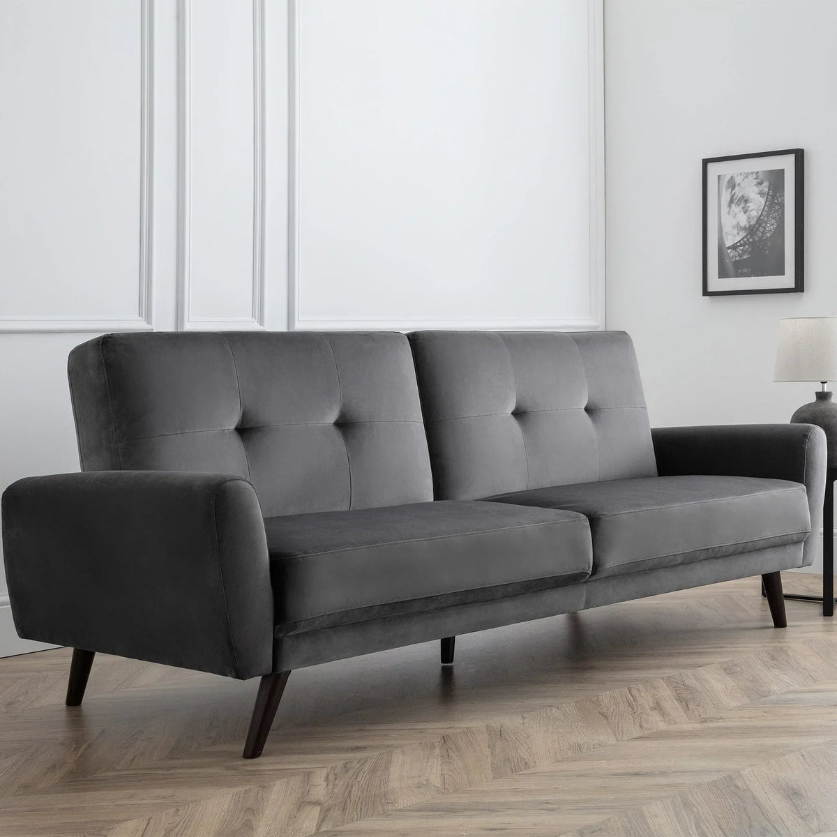 Grey velvet sofabed with button-tufted backrest in modern living room with wood flooring
