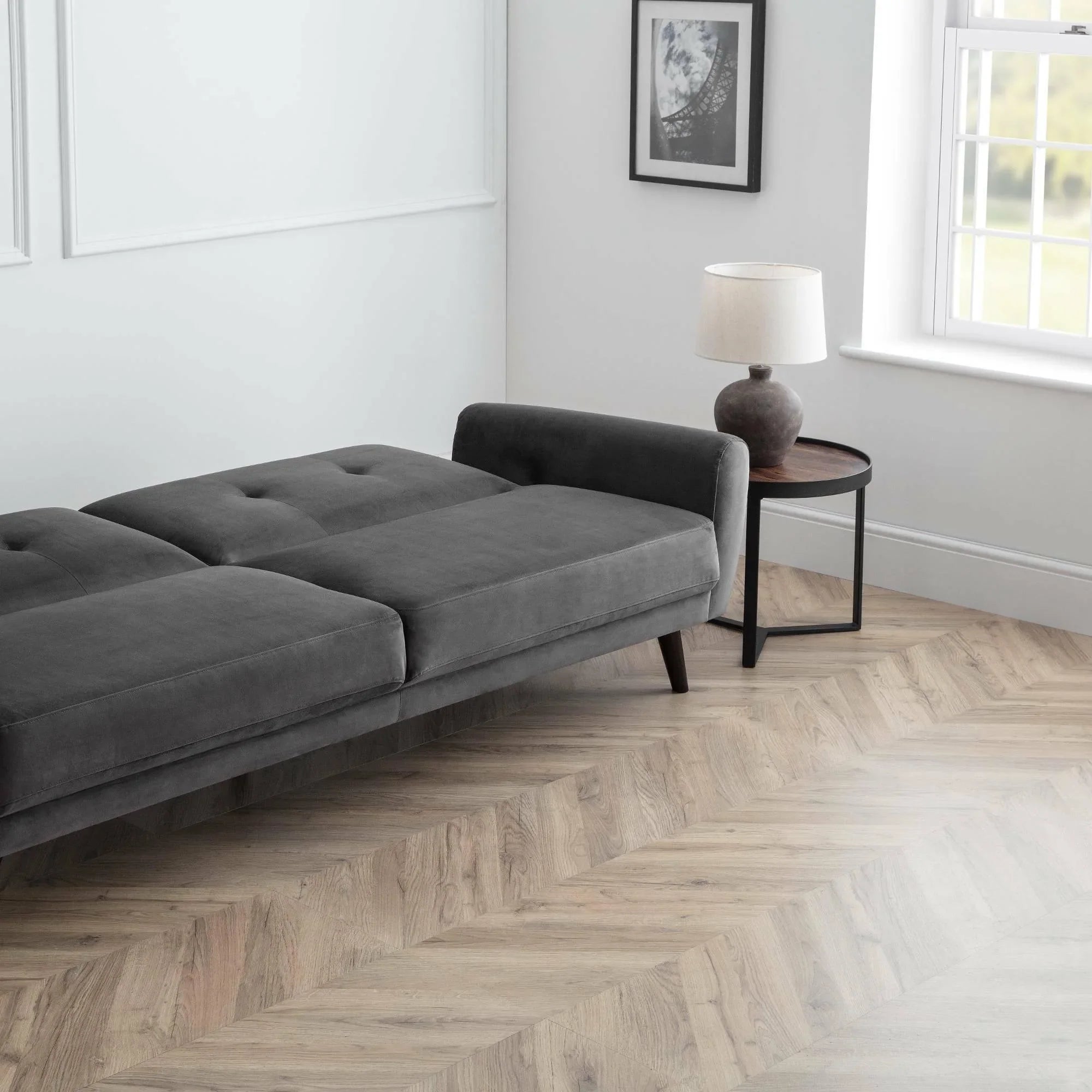 Grey velvet sofabed fully extended in modern room with side table and lamp