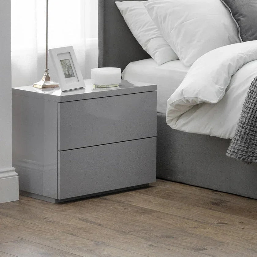 Grey two drawer bedside table beside bed on wooden floor with lamp and decor