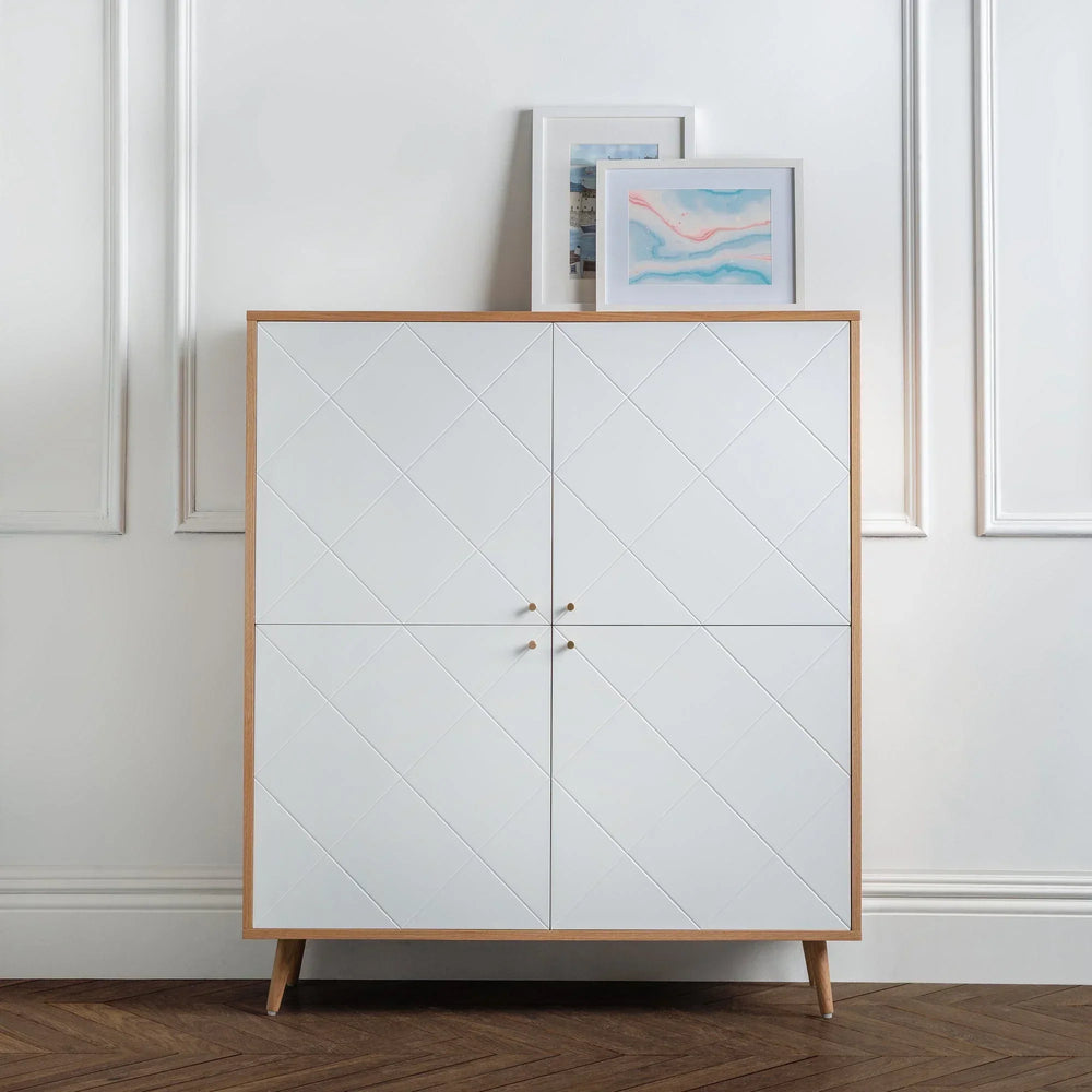 White modern cabinet with oak frame and diagonal pattern doors, two framed prints on top