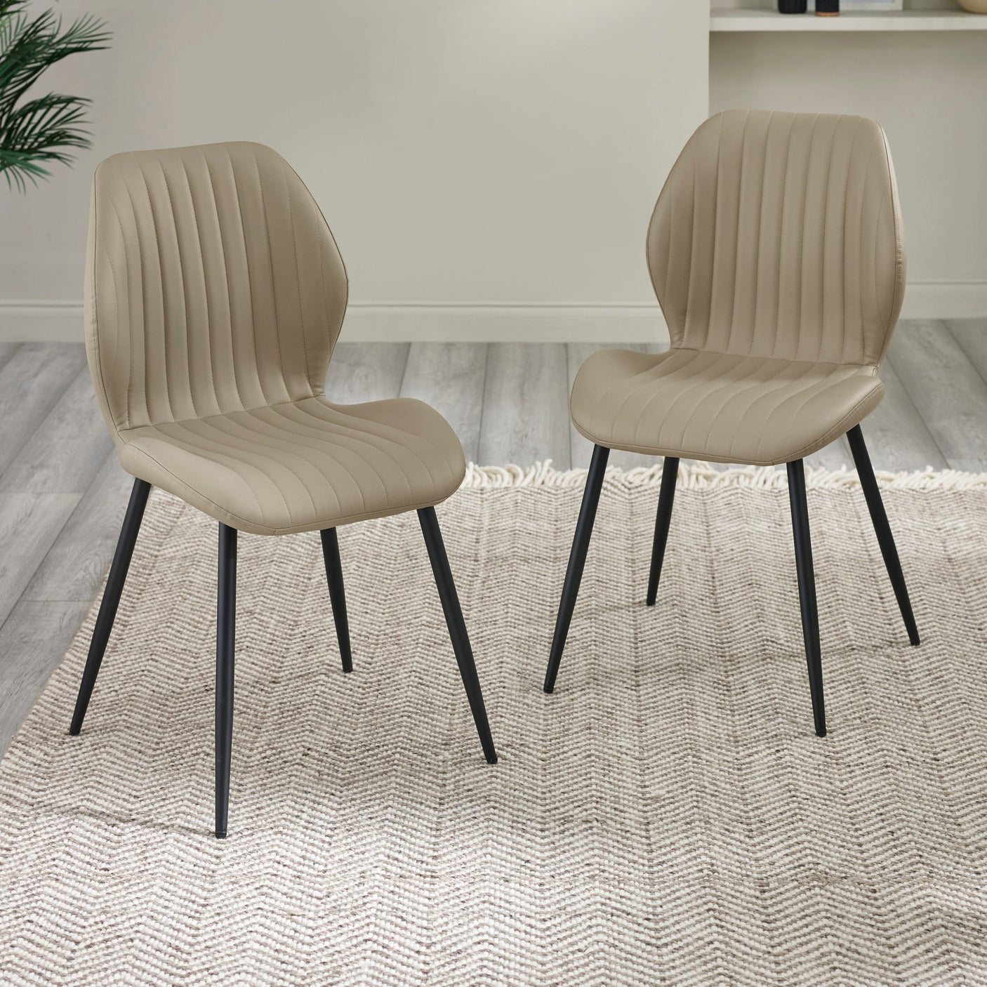 Two beige upholstered dining chairs with curved backs and black metal legs on beige patterned rug