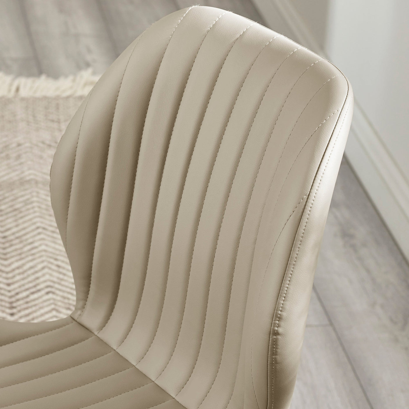 Close-up of beige chair backrest upholstery with vertical stitching on light wood floor