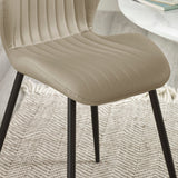 Close-up of beige upholstered dining chair with stitched vertical lines and black metal legs on textured rug.