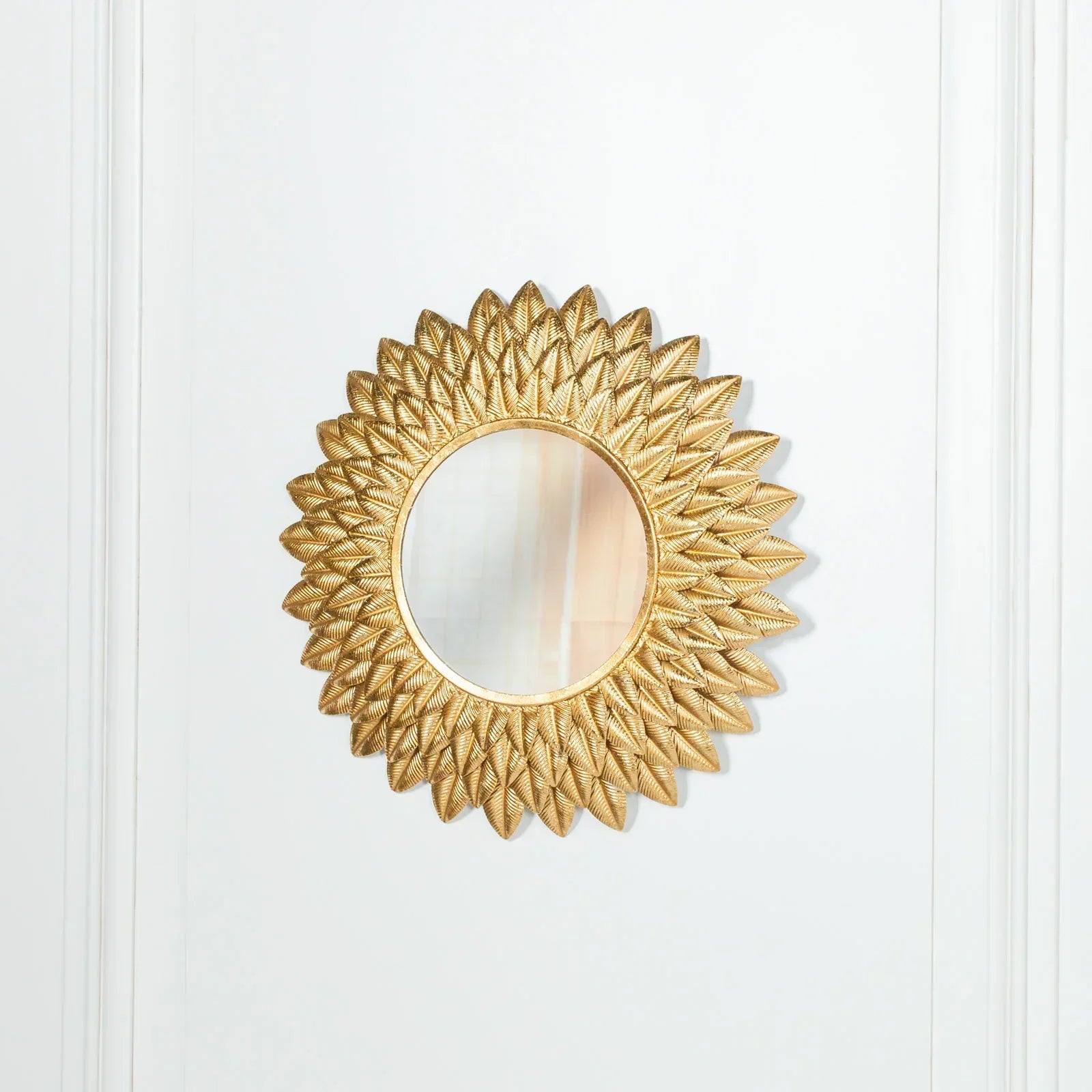 Gold sunburst wall mirror with textured frame on white panelled wall