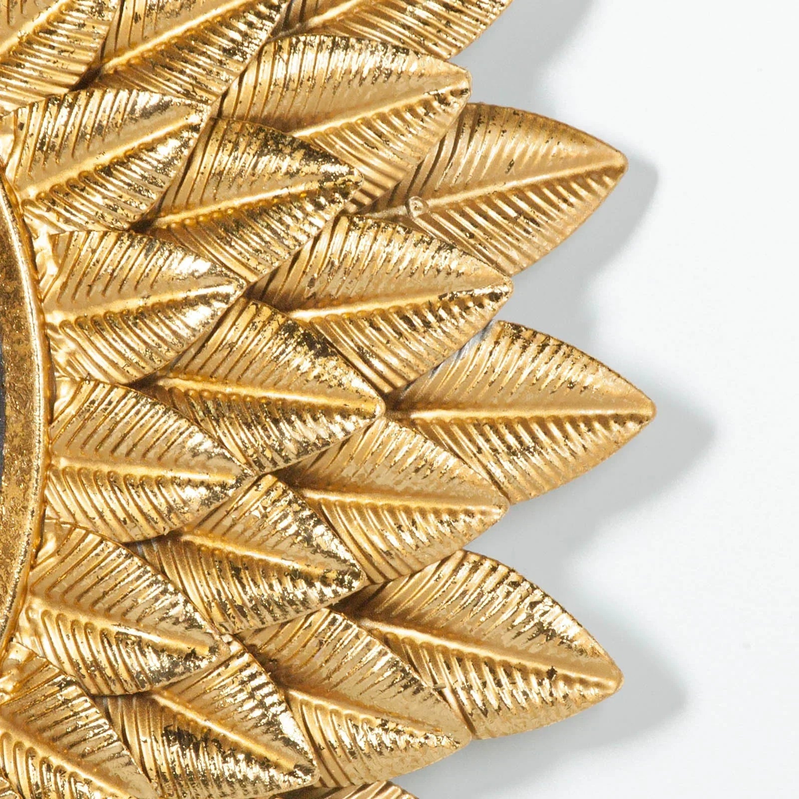 Gold metal wall mirror frame with textured leaf pattern, close-up corner view
