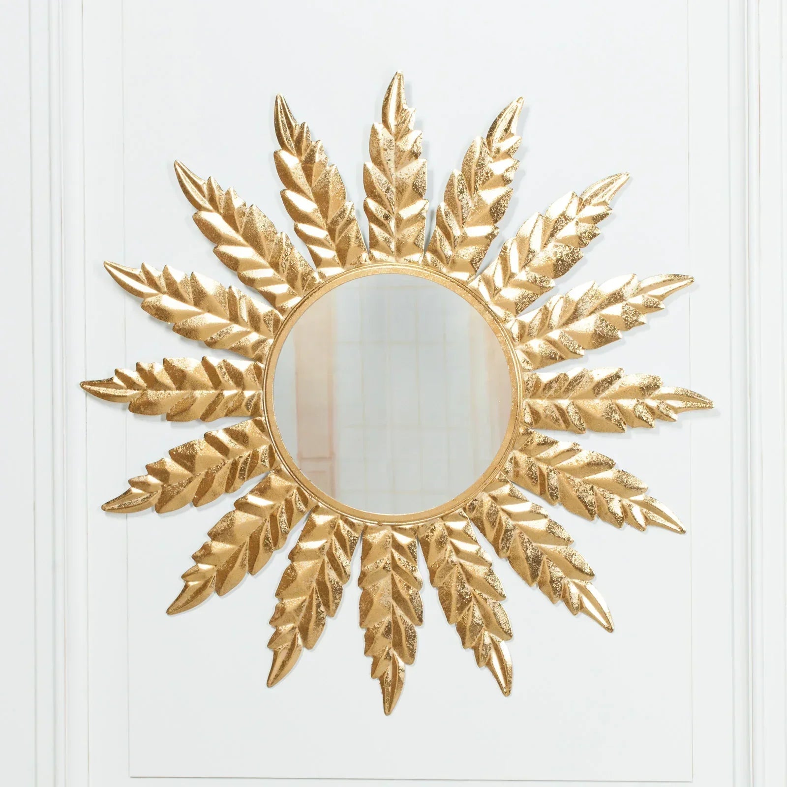 Gold sunburst wall mirror with textured leaf design against white panel background