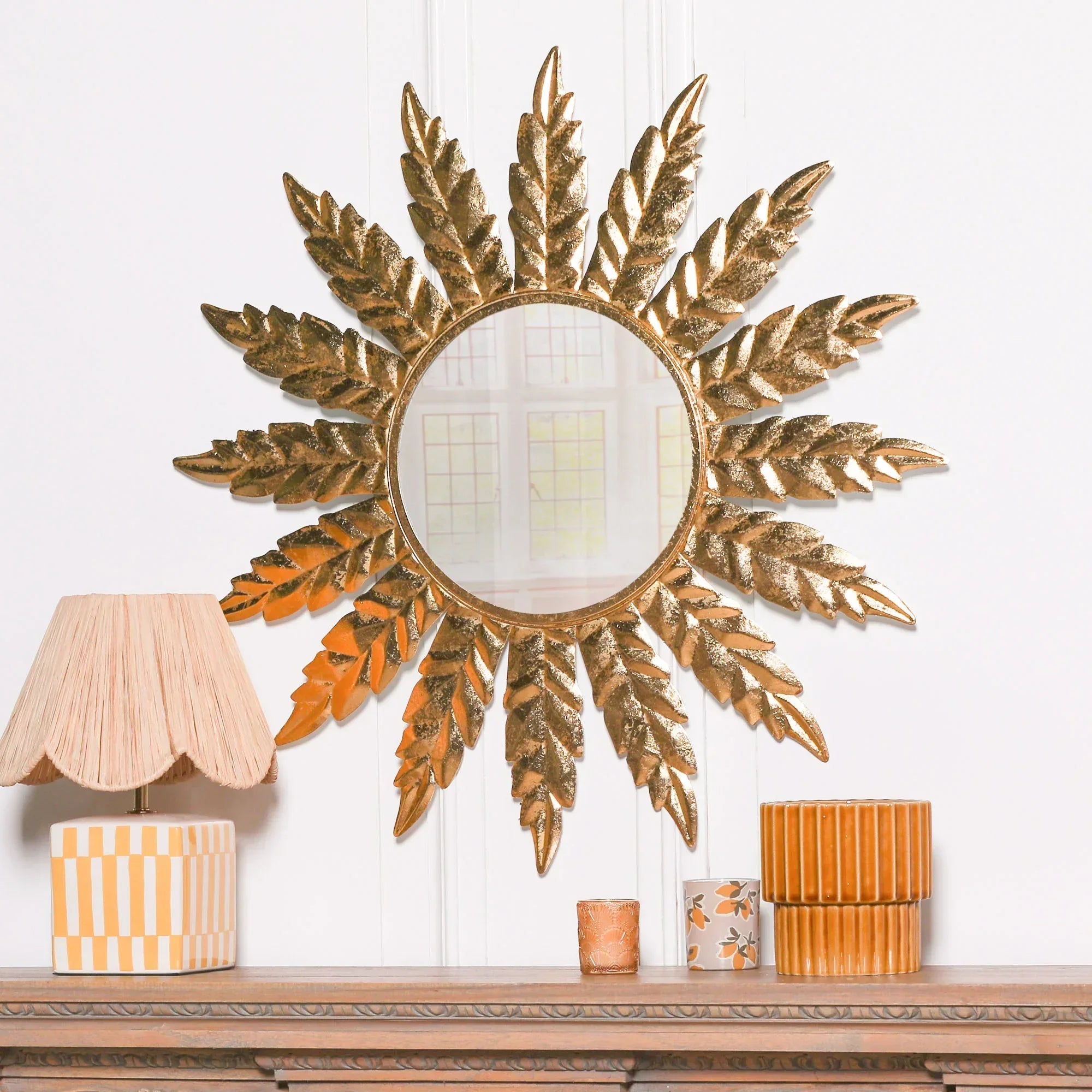 Gold leaf decorative wall mirror above mantel with orange ceramic home decor