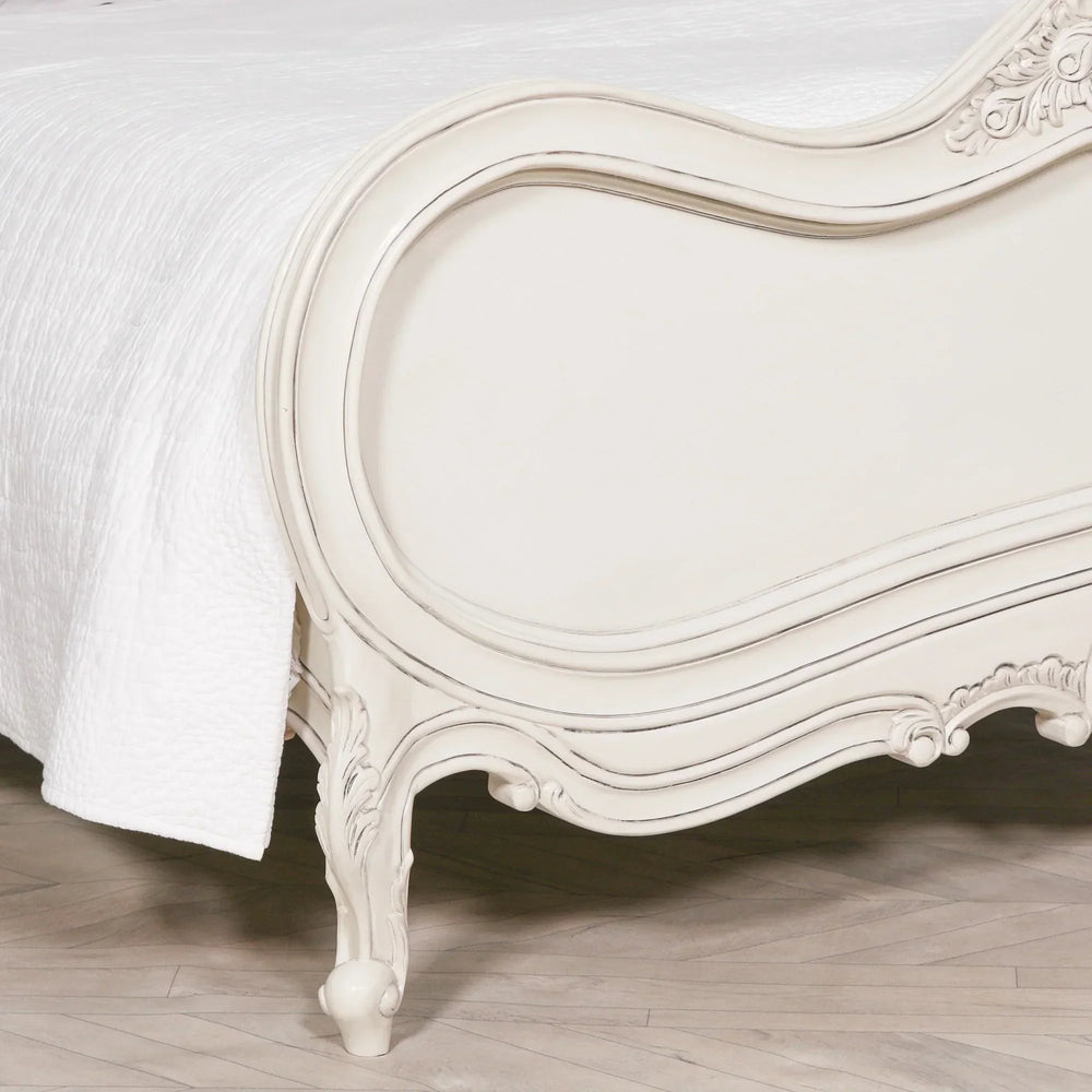 Cream wood bed frame with carved detailing and white quilted bedding on herringbone floor