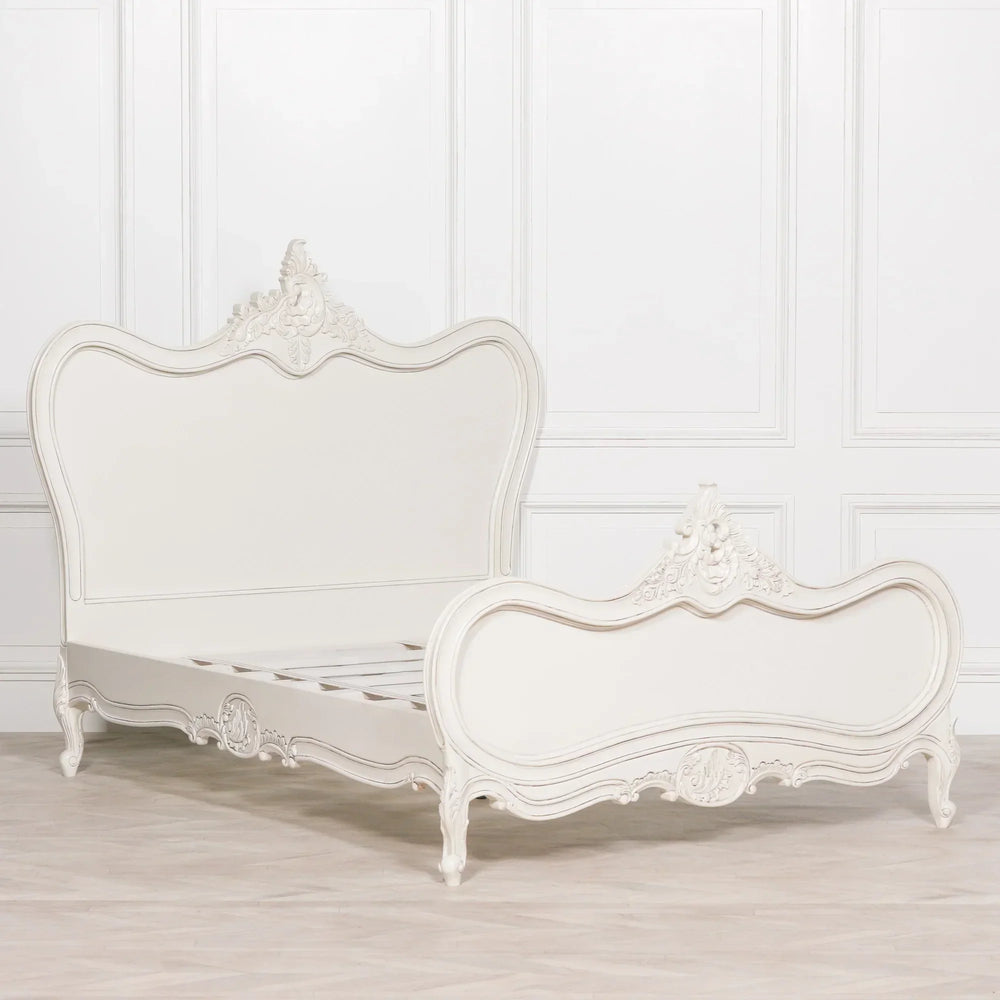 Ivory wooden bed frame with ornate carved headboard and footboard on light wood floor