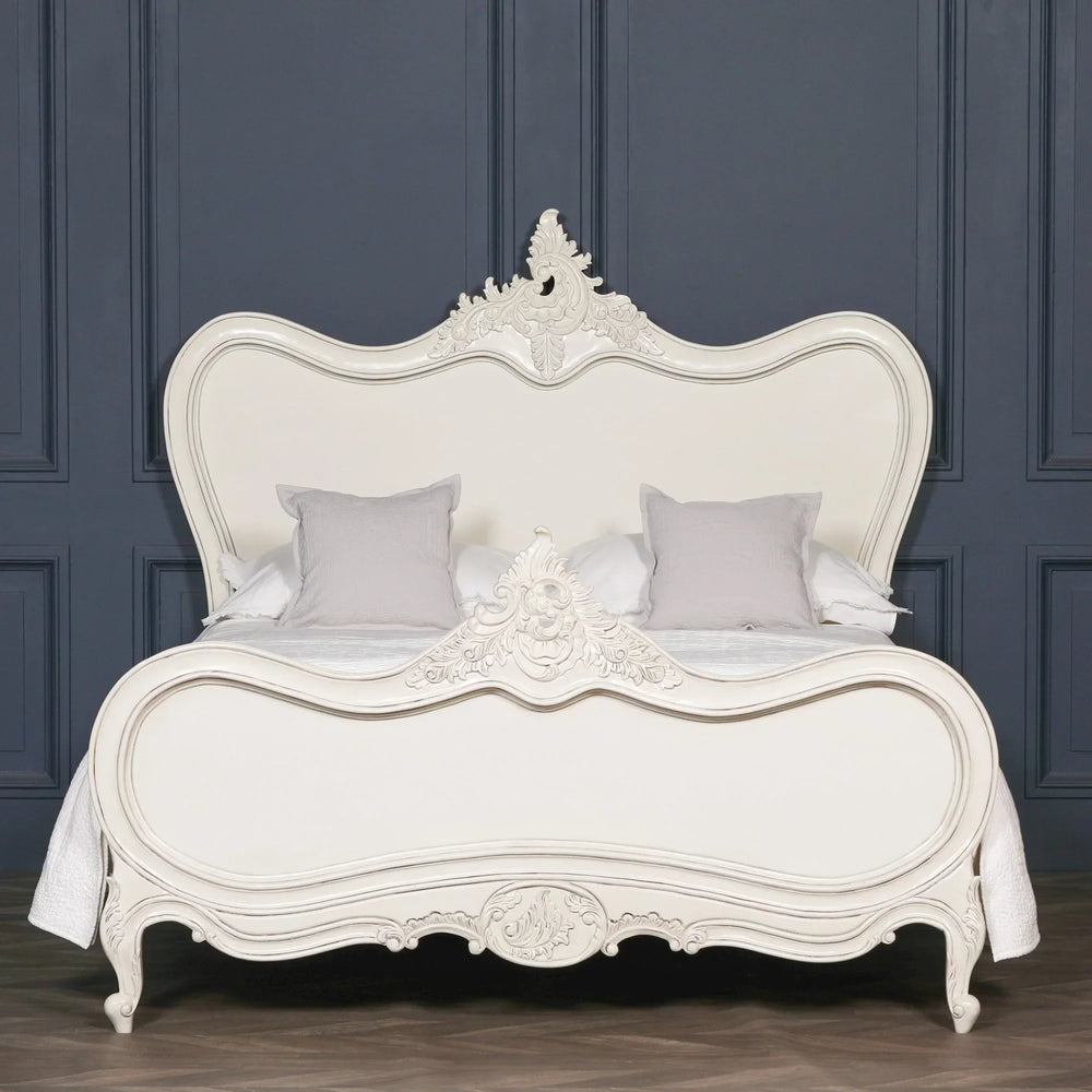 French style cream bed with ornate carved headboard and footboard against dark wall