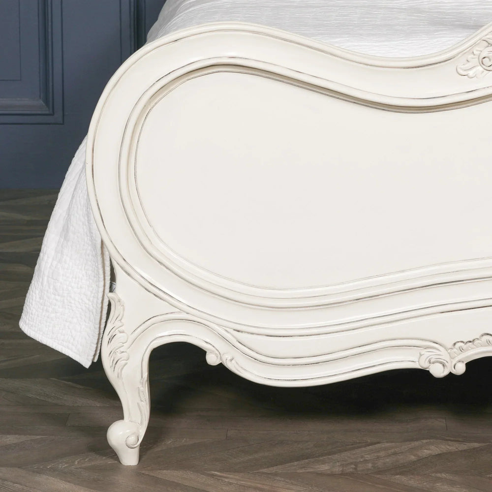 Ivory painted wooden bed frame with curved detailing and carved legs on wood flooring