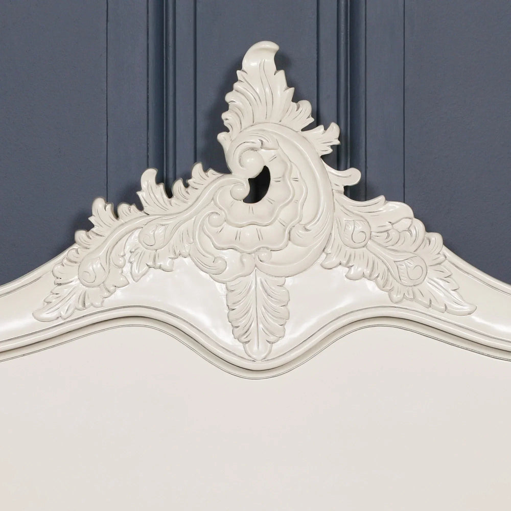 Ivory wooden bed headboard with ornate carved detail against dark panelled wall