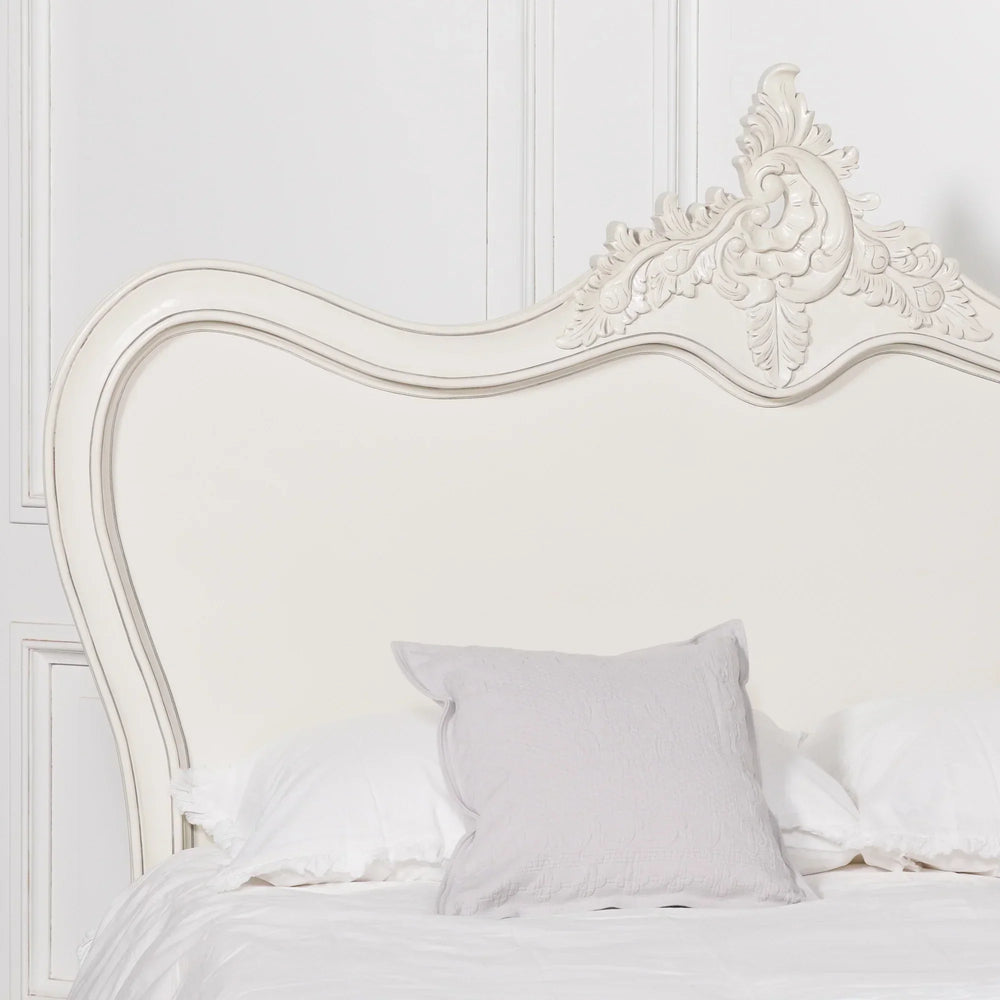 Ivory wooden bed with ornate carved headboard and white bedding in classic bedroom setting