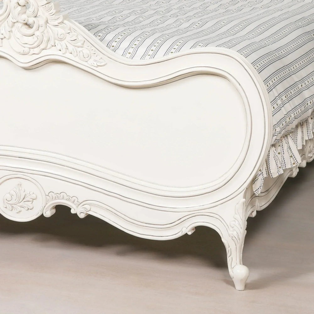 White carved wooden bed frame with ornate detailing and patterned bedding