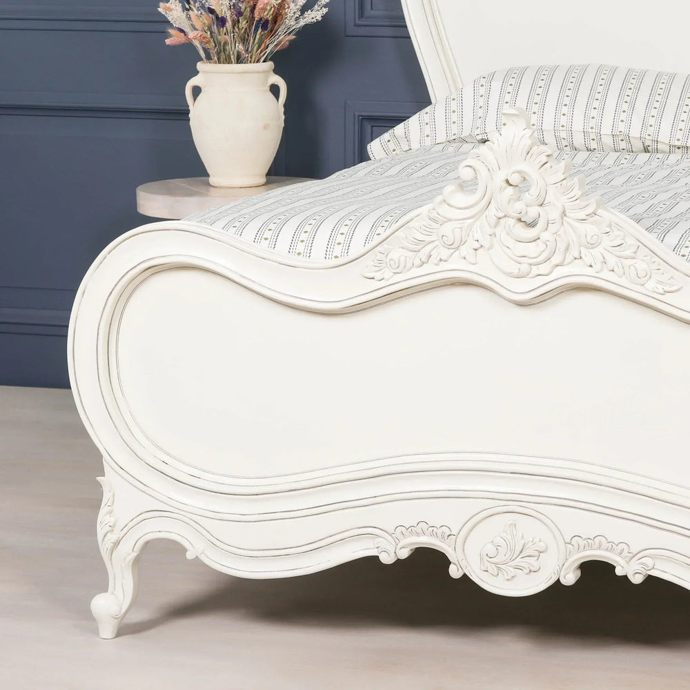Ivory French style bed frame with ornate carved wood detail and striped bedding