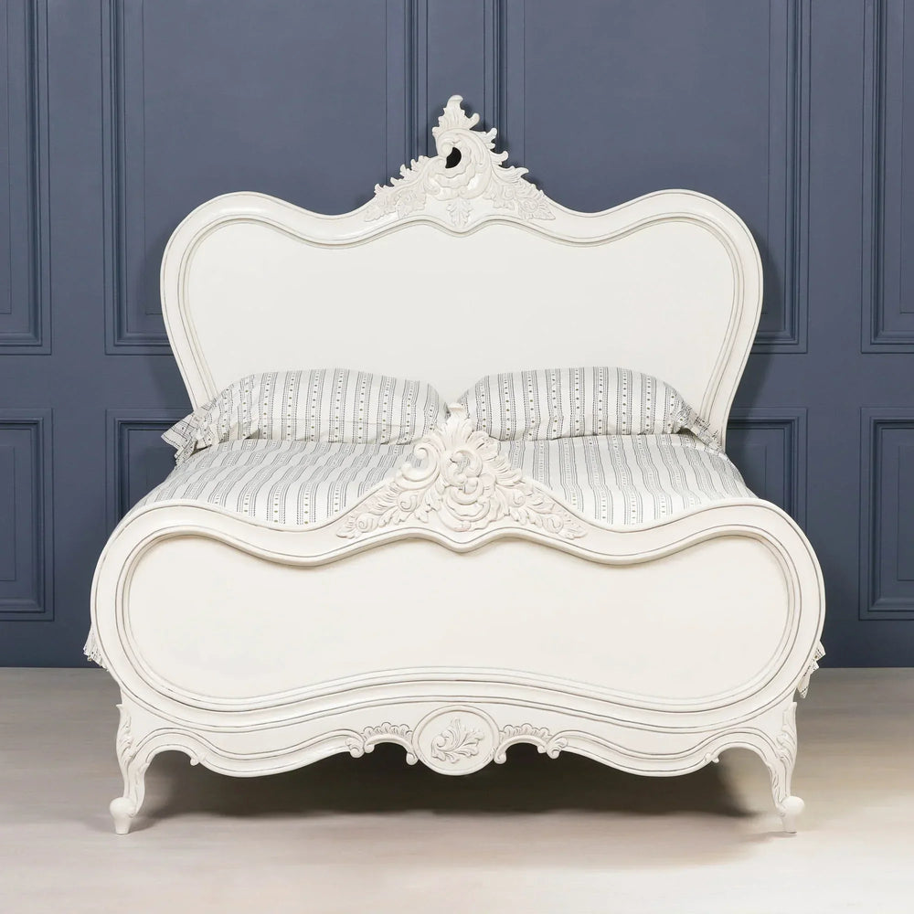 White carved wooden bed frame with ornate headboard and footboard against navy wall