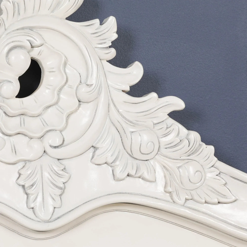 White carved wooden headboard with ornate floral and leaf detail against blue wall