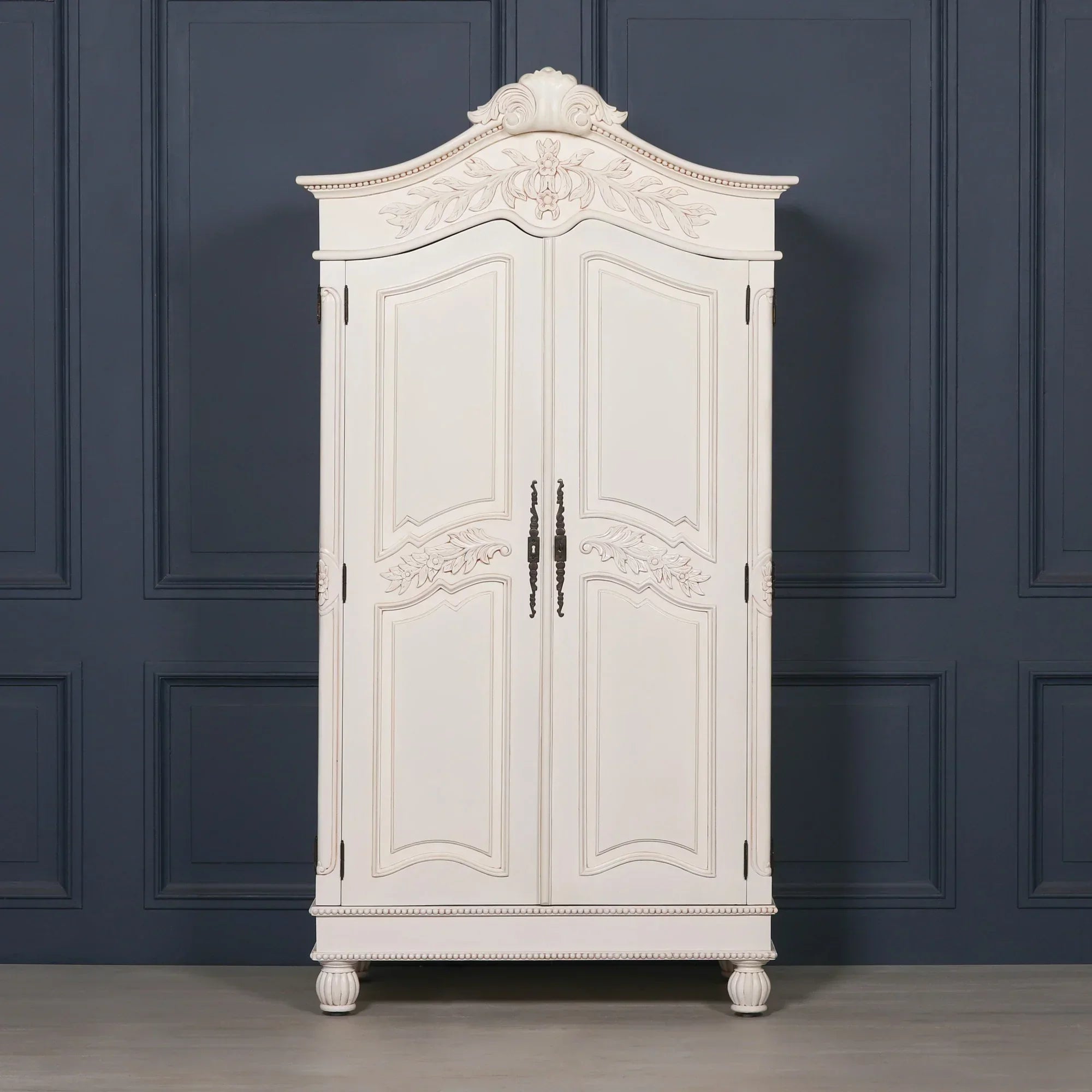White wooden wardrobe with ornate carved detailing and double doors against dark panel wall