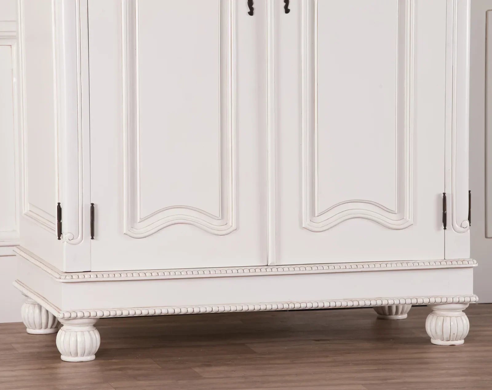 White wooden wardrobe base with carved legs and decorative beading on timber floor
