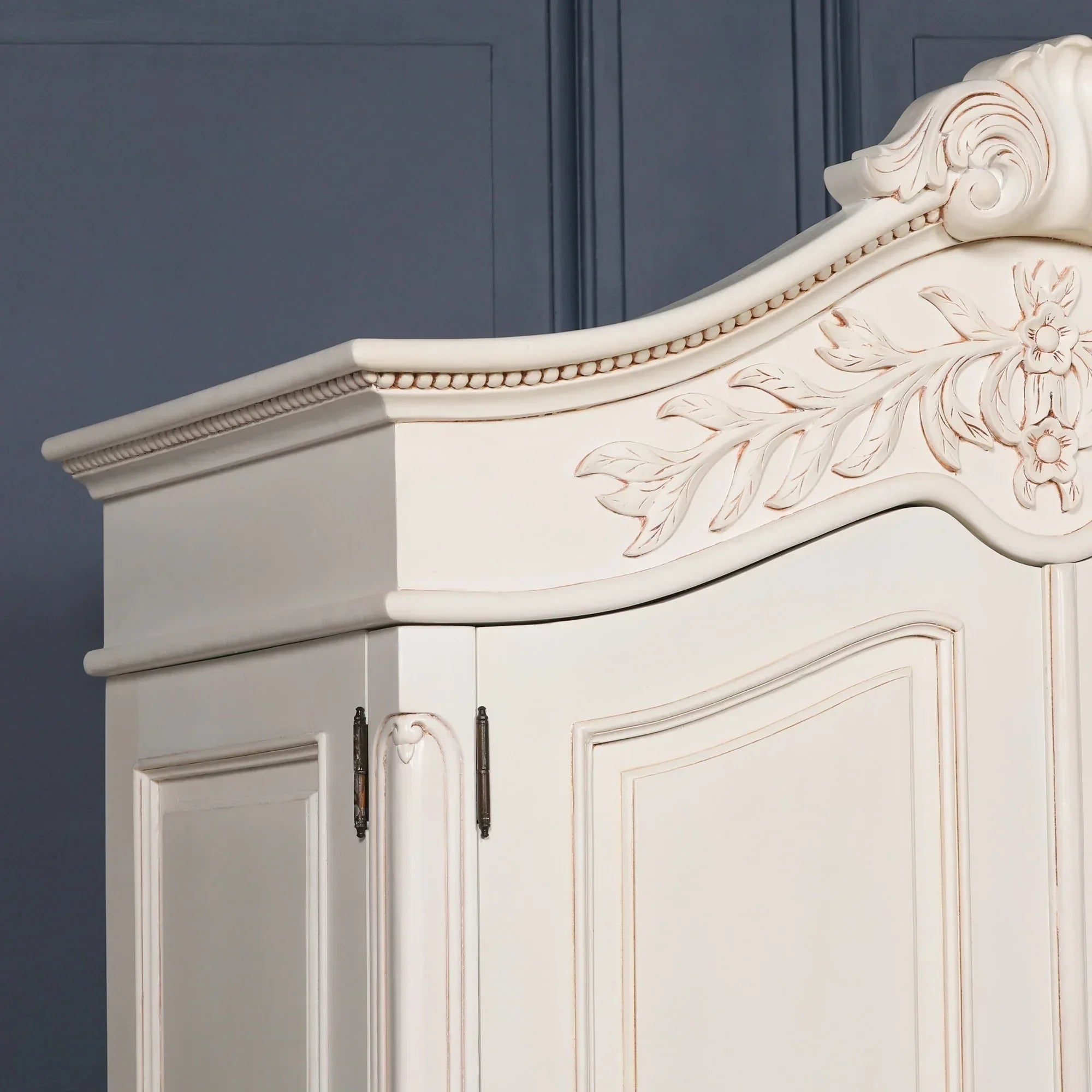 Cream wooden wardrobe with floral carved detail and ornate molding on top corner view