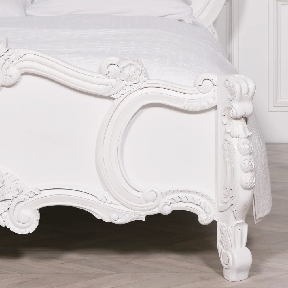 White carved wooden bed frame with ornate detailing and curved legs on hardwood floor