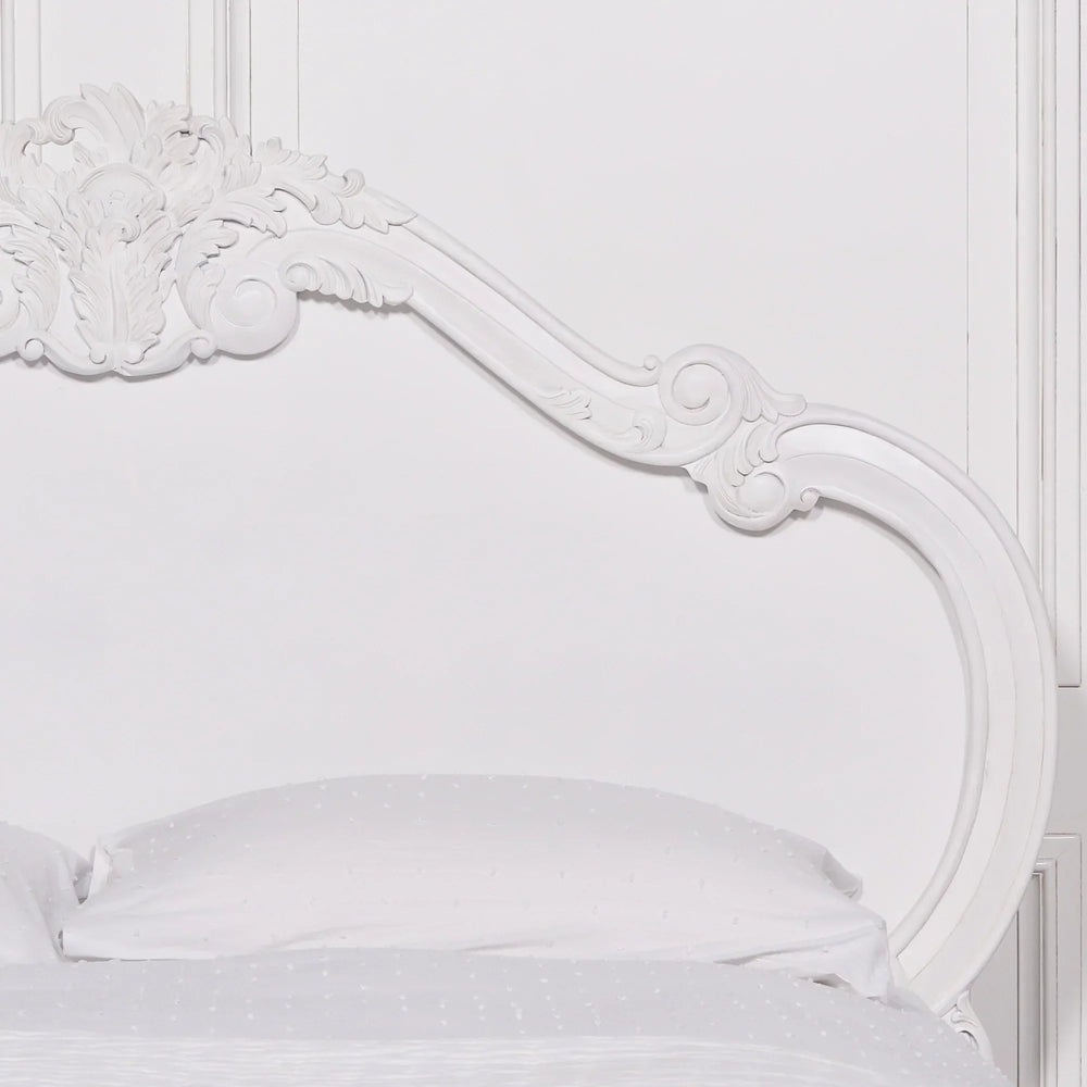 White carved wooden bed frame with ornate headboard detail and white bedding