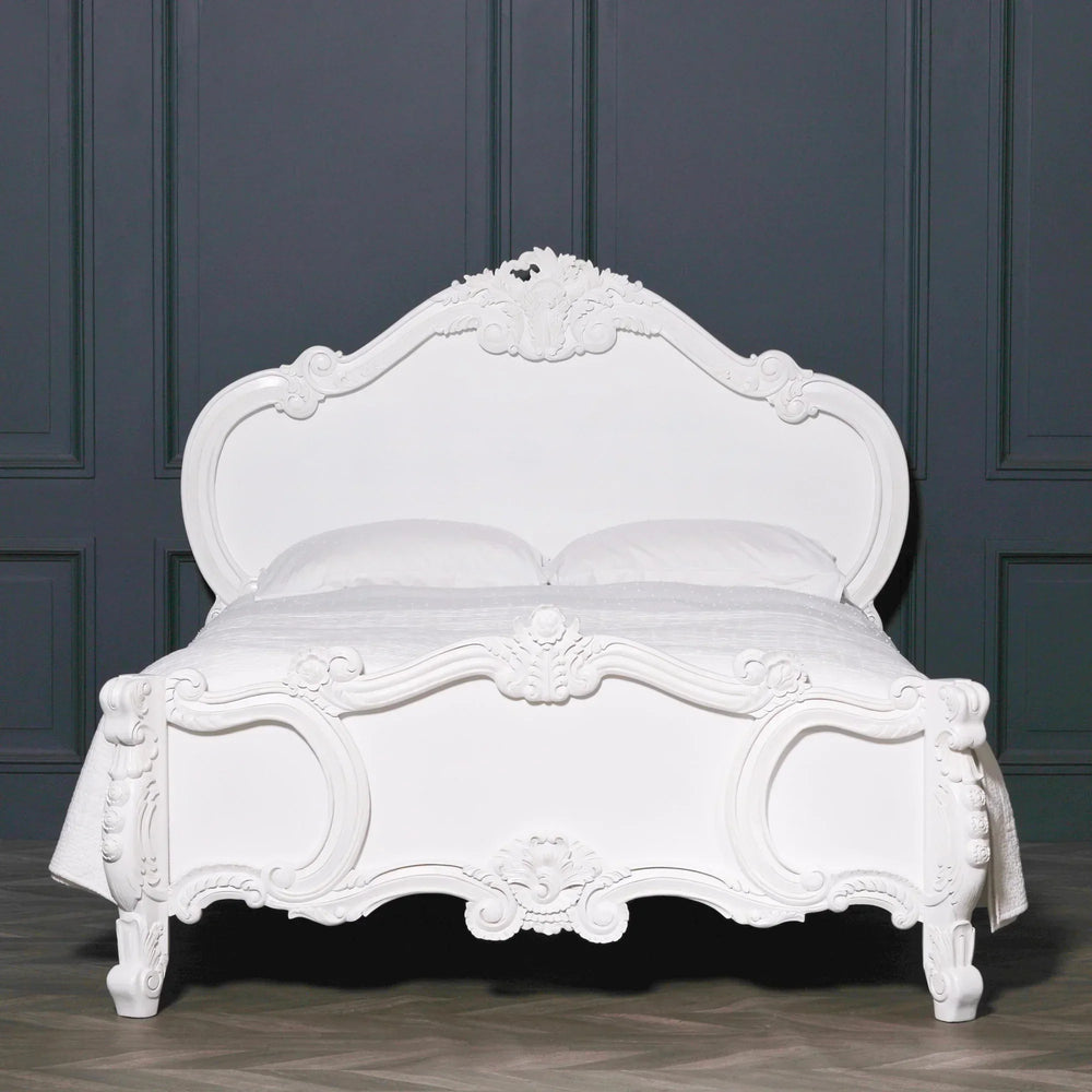 White carved wooden bed frame with ornate details against dark wall