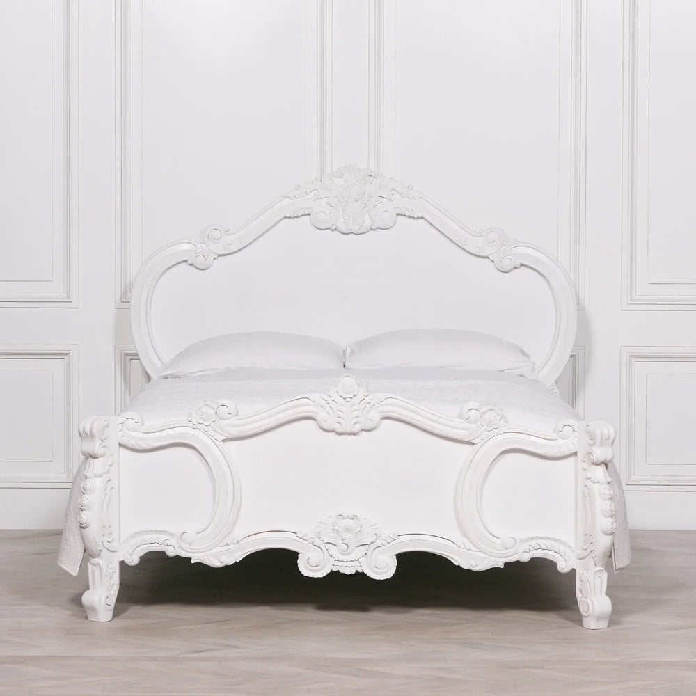 White carved wooden bed frame with ornate detailing and matching white bedding