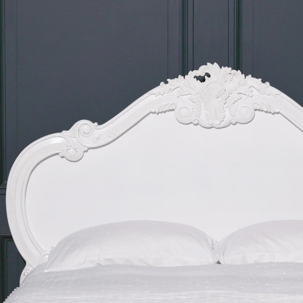 White carved wood bed frame headboard with ornate detailing against dark panel wall