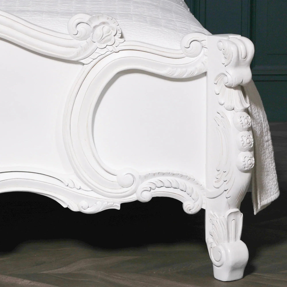 White carved wood bed footboard with ornate detailing on dark wooden floor