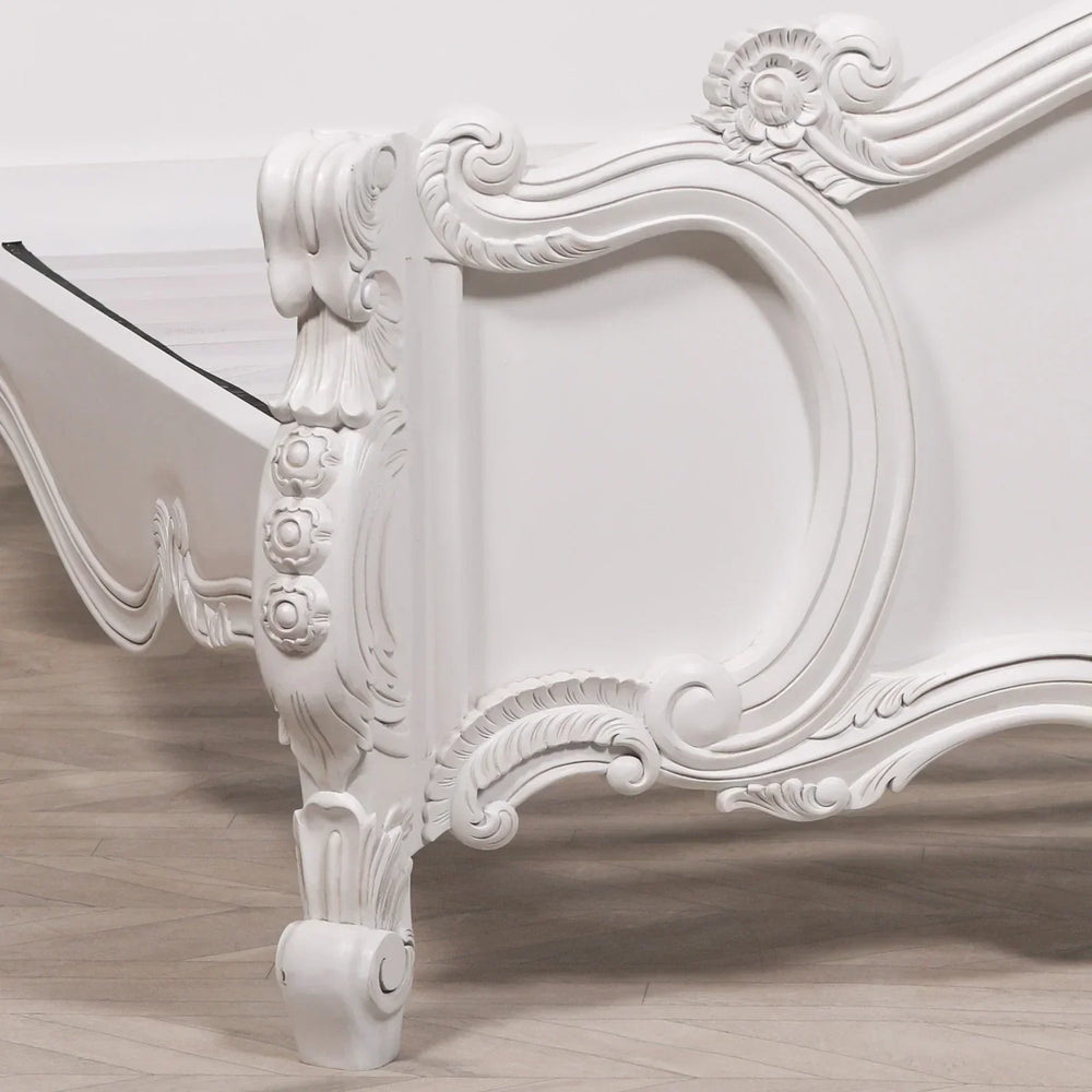 White carved wood bed frame corner with intricate floral detailing on leg and panel