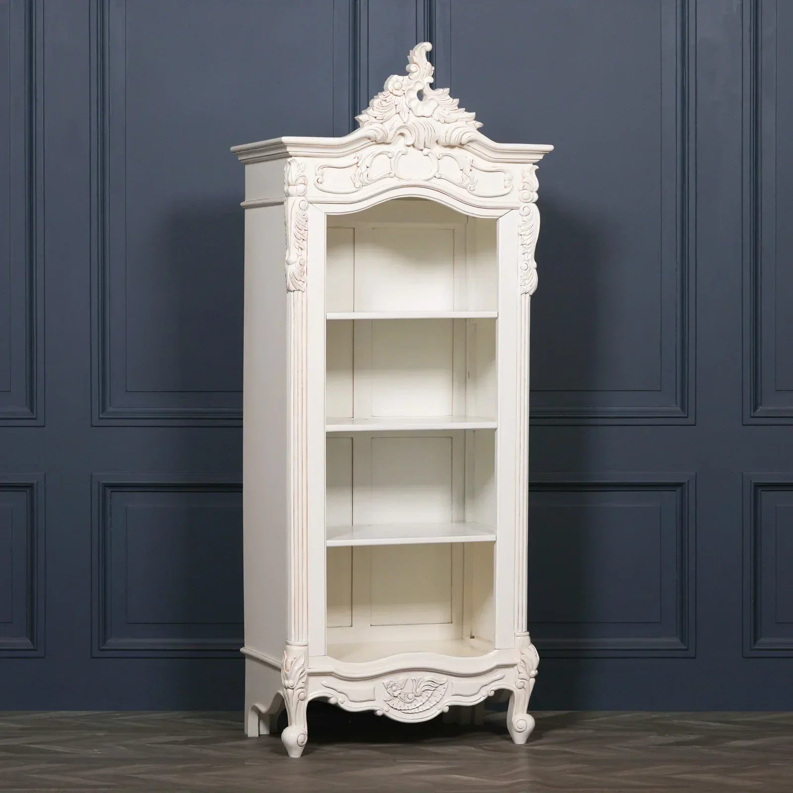 White wooden display cabinet with carved detailing and open shelving against blue wall