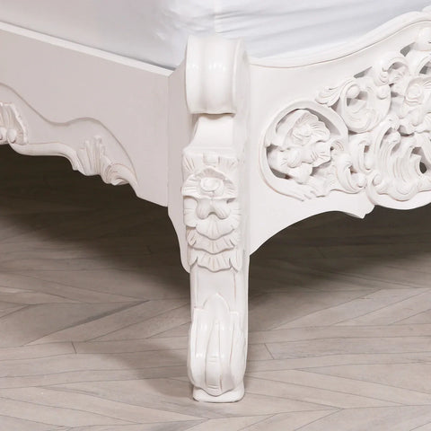 White carved wooden bed leg with ornate floral detailing on light wood floor
