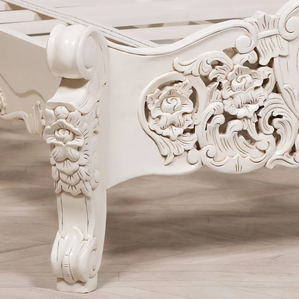 Carved white wooden bed frame corner with floral detailing on leg and side