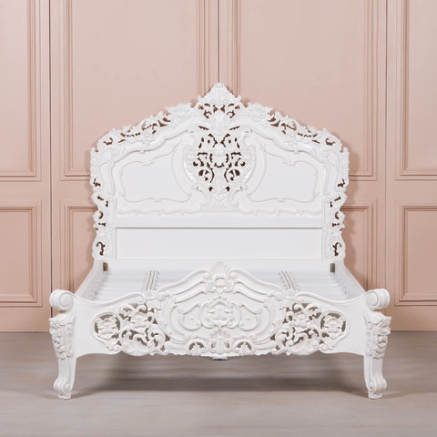 White ornate bed against a pink paneled wall