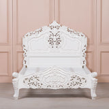 White ornate bed against a pink paneled wall