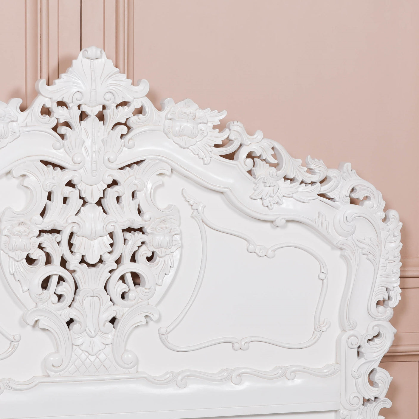 Decorative white headboard with intricate carvings against a pink wall.